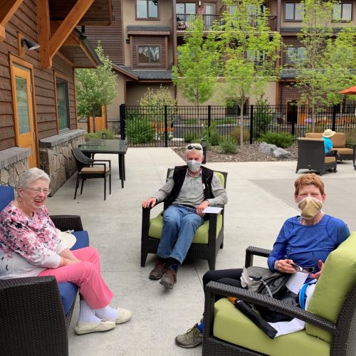 Courtyard at Origin at Spring Creek, with a young boy, a senior woman, and a senior man sitting on patio chairs, wearing face masks, looking at the camera