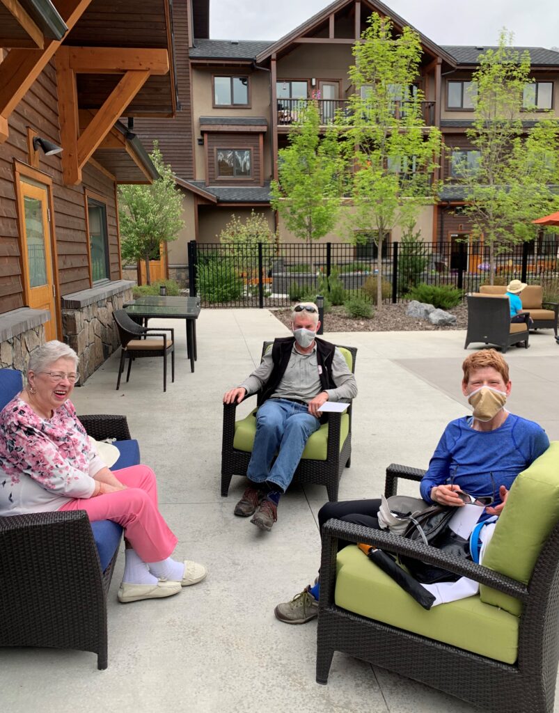 Courtyard at Origin at Spring Creek, with a young boy, a senior woman, and a senior man sitting on patio chairs, wearing face masks, looking at the camera 