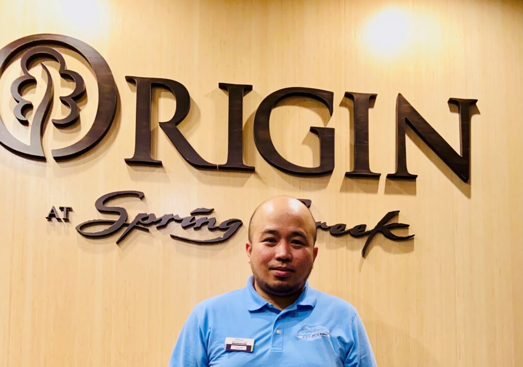 Louie standing in front of an Origin at Spring Creek sign