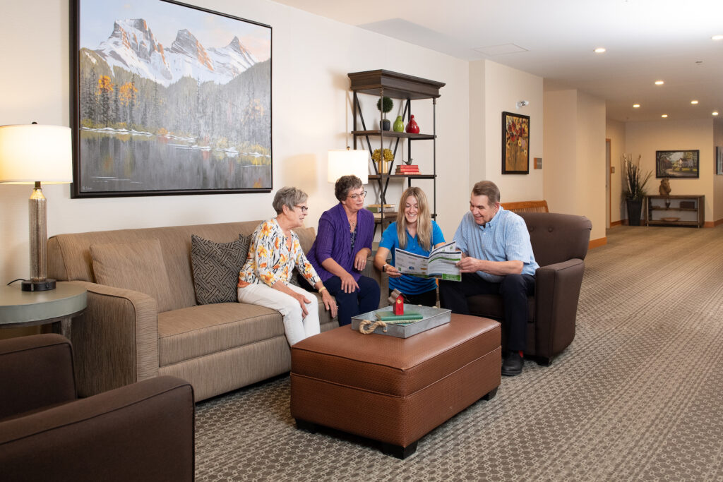 Three senior residents and a younger adult companion chat in a comfortable living space at Origin at Spring Creek.